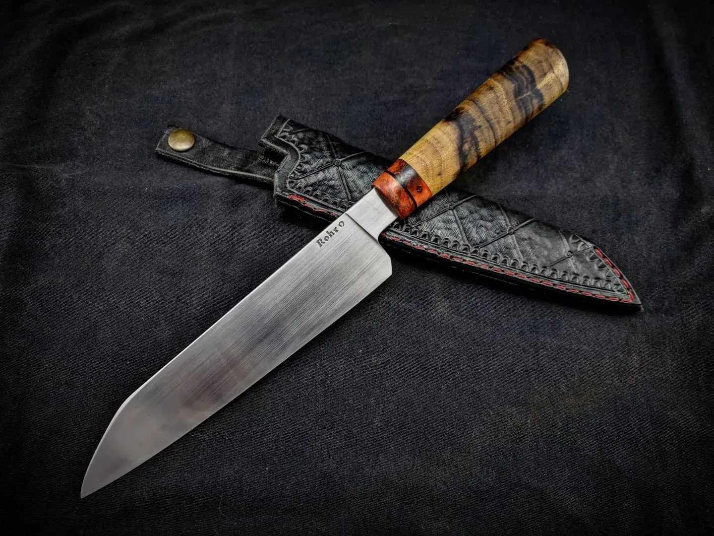 Cuchillo tipo gyuto con cabo de acacia negra junto a su vaina de cuero labrado