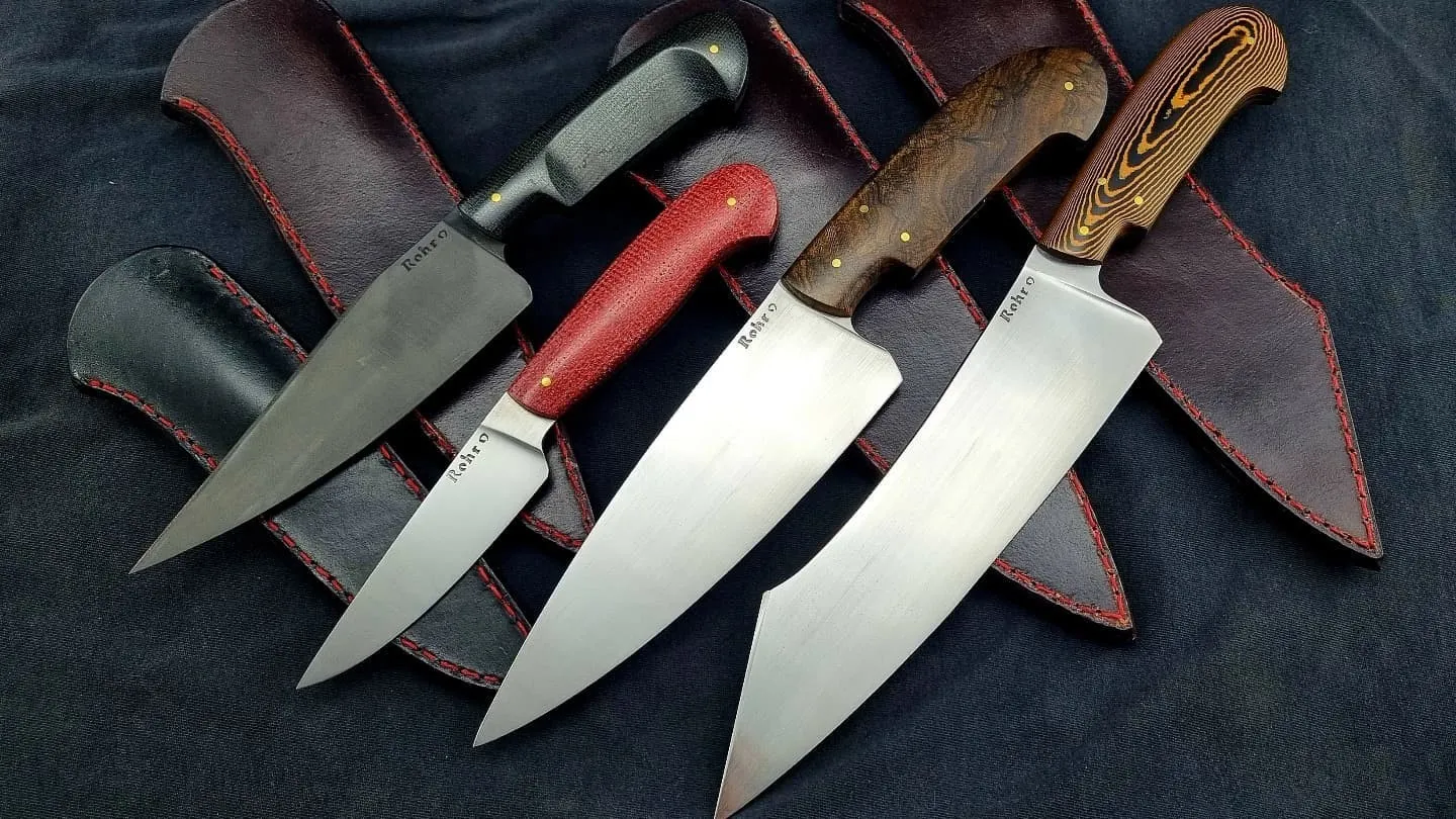 Cuatro cuchillos con cabos de madera y micarta apoyados sobre sus vainas de cuero